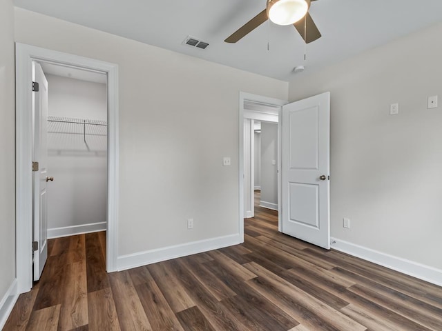 unfurnished bedroom with dark wood-style floors, a walk in closet, a closet, visible vents, and baseboards