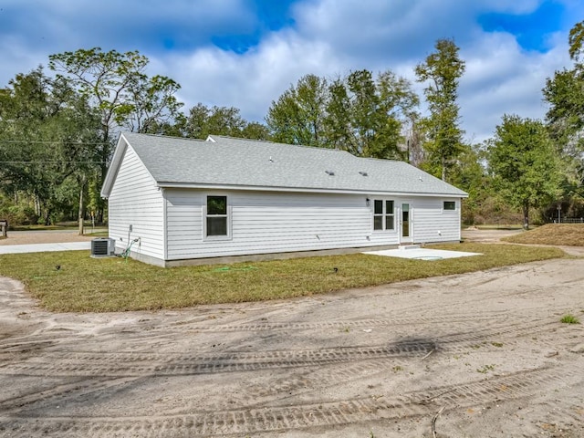 rear view of property with a shingled roof, a patio area, central AC, and a lawn