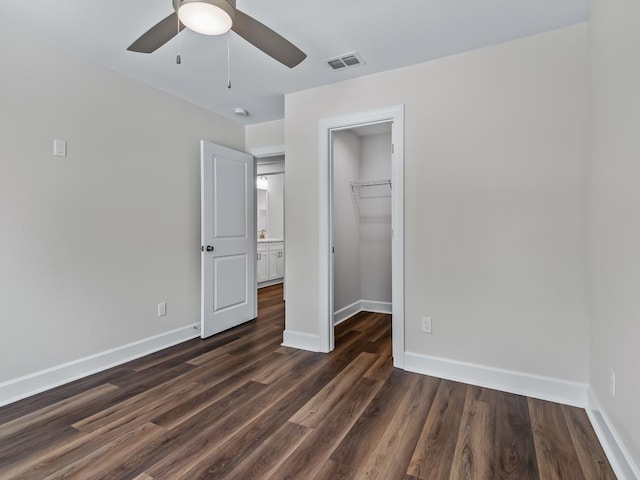 unfurnished bedroom featuring baseboards, visible vents, dark wood-type flooring, a walk in closet, and a closet