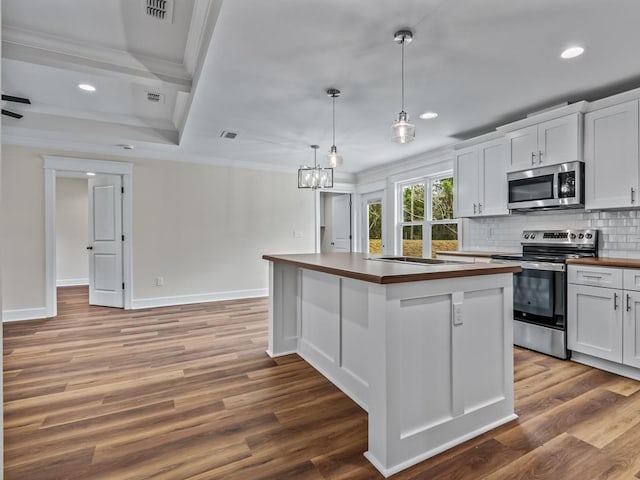 kitchen featuring butcher block countertops, white cabinetry, ornamental molding, appliances with stainless steel finishes, and a center island