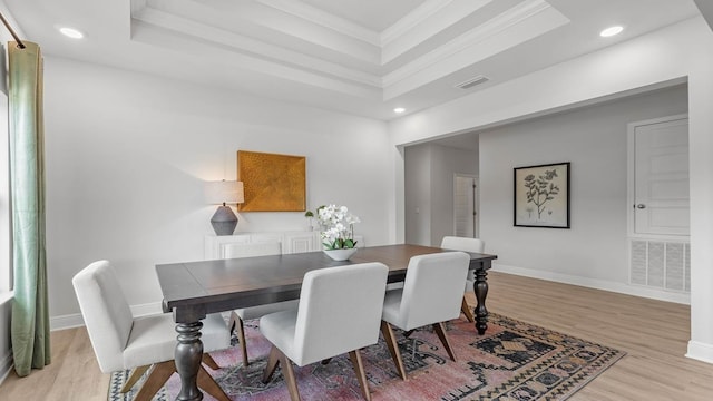 dining room with a tray ceiling, crown molding, and light wood-type flooring