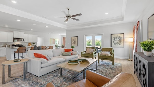 living room with ceiling fan, light wood-type flooring, crown molding, and a tray ceiling