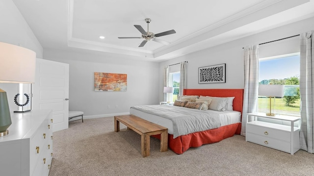 carpeted bedroom with a tray ceiling, multiple windows, ceiling fan, and crown molding