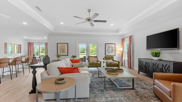 living room featuring crown molding, french doors, light hardwood / wood-style flooring, and a tray ceiling