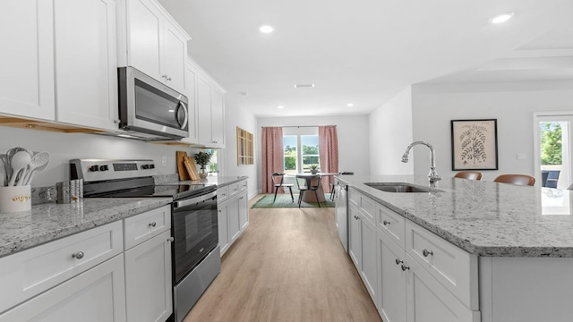 kitchen with stainless steel appliances, sink, a center island with sink, light hardwood / wood-style flooring, and white cabinets