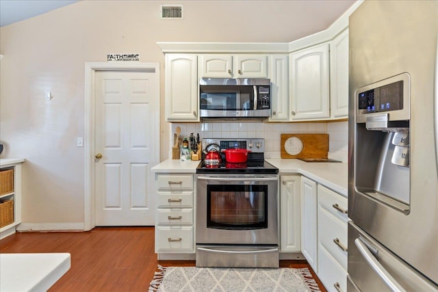 kitchen with decorative backsplash, white cabinets, light wood-type flooring, and appliances with stainless steel finishes