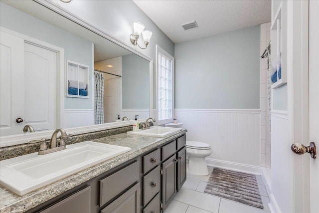 bathroom with a wainscoted wall, a textured ceiling, visible vents, and a sink