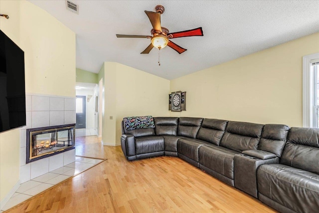 living area with ceiling fan, a fireplace, visible vents, vaulted ceiling, and light wood finished floors