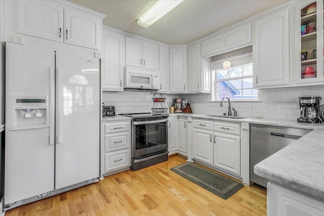 kitchen with white cabinets, glass insert cabinets, stainless steel appliances, light countertops, and a sink