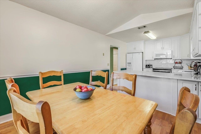 dining room with visible vents, vaulted ceiling, light wood-style flooring, and baseboards