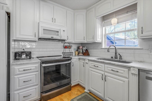 kitchen with white cabinets, light wood-style floors, stainless steel appliances, and a sink