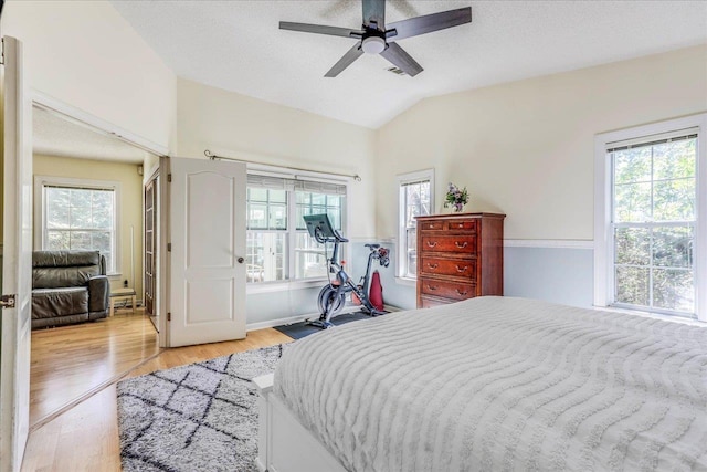 bedroom with light wood-type flooring, ceiling fan, lofted ceiling, and a textured ceiling