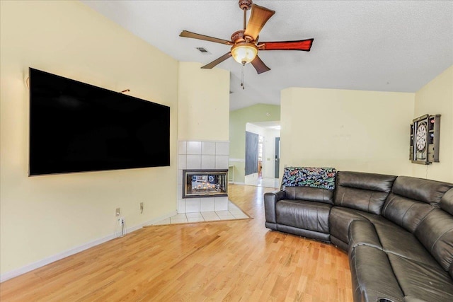 living room featuring lofted ceiling, a tile fireplace, a ceiling fan, baseboards, and light wood finished floors