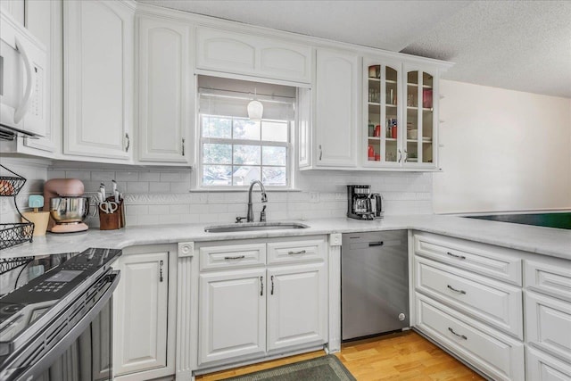 kitchen featuring stainless steel appliances, light countertops, glass insert cabinets, white cabinetry, and a sink