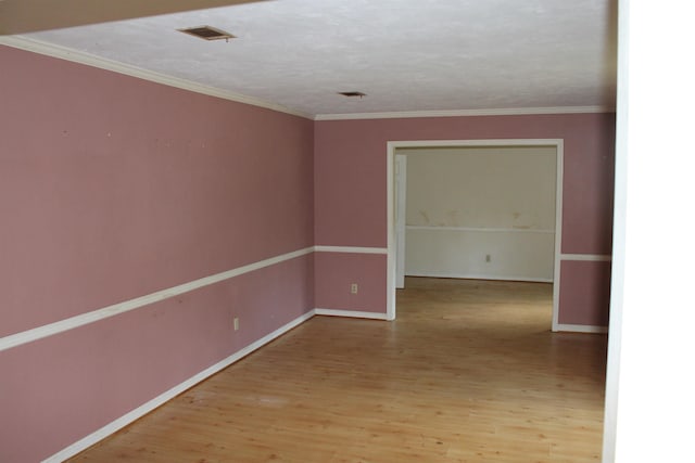 empty room featuring baseboards, visible vents, wood finished floors, and ornamental molding