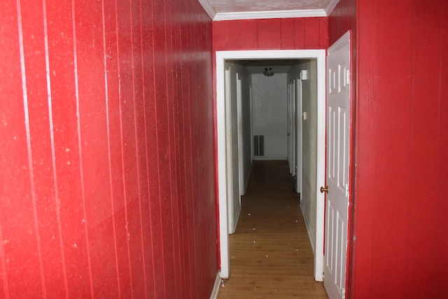 hallway featuring wood walls, wood finished floors, visible vents, and crown molding