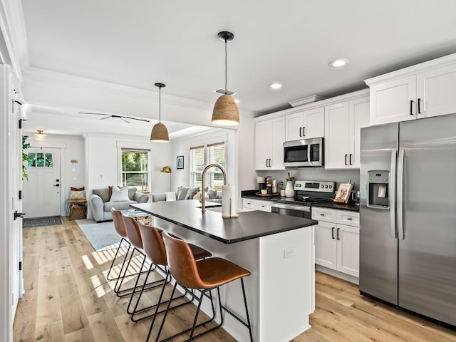 kitchen with pendant lighting, a center island with sink, light wood-type flooring, white cabinetry, and stainless steel appliances