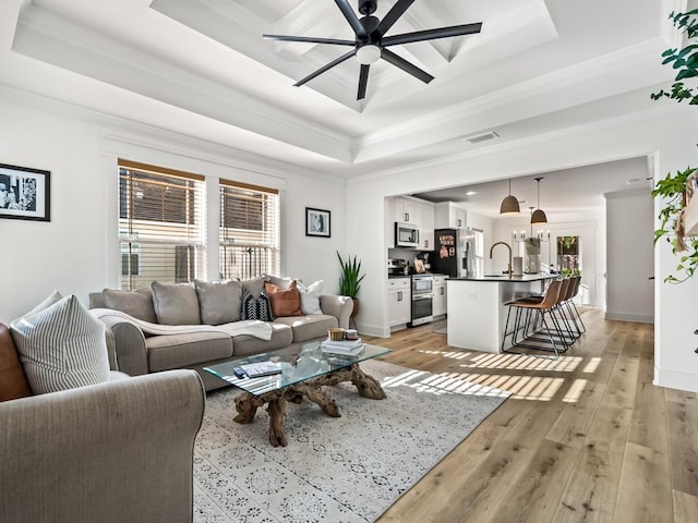 living room with light wood-type flooring, a tray ceiling, ceiling fan, and ornamental molding