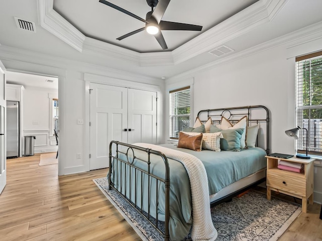 bedroom featuring light wood-type flooring, a raised ceiling, ceiling fan, crown molding, and fridge