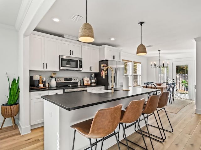 kitchen with white cabinets, appliances with stainless steel finishes, decorative light fixtures, and a kitchen island with sink