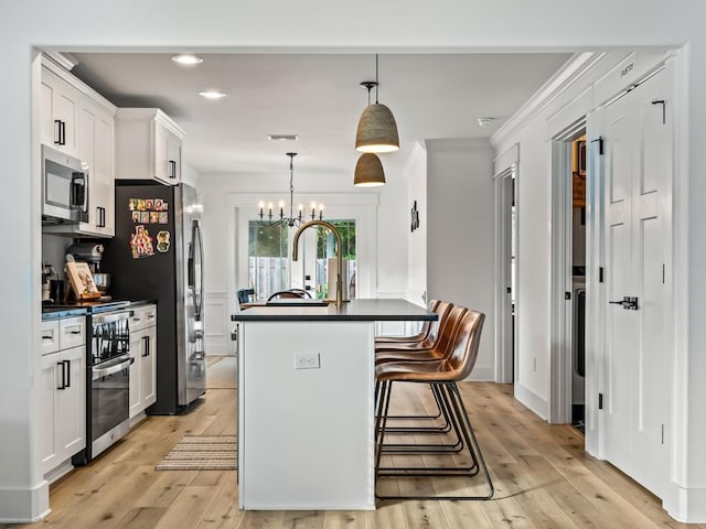 kitchen with white cabinets, appliances with stainless steel finishes, decorative light fixtures, and light hardwood / wood-style floors