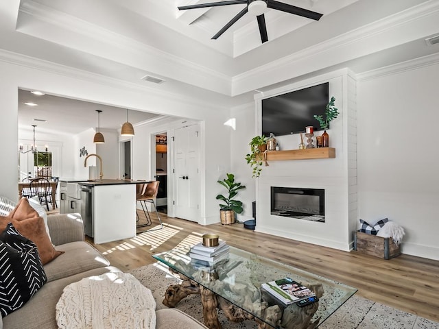 living room with ceiling fan with notable chandelier, a large fireplace, light hardwood / wood-style flooring, and crown molding