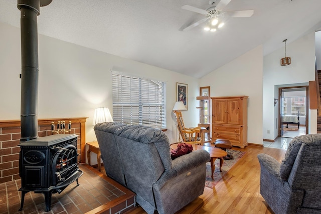 living area featuring a ceiling fan, wood finished floors, baseboards, high vaulted ceiling, and a wood stove