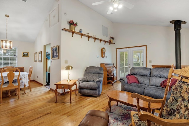 living room with ceiling fan with notable chandelier, french doors, light wood-style floors, baseboards, and a wood stove