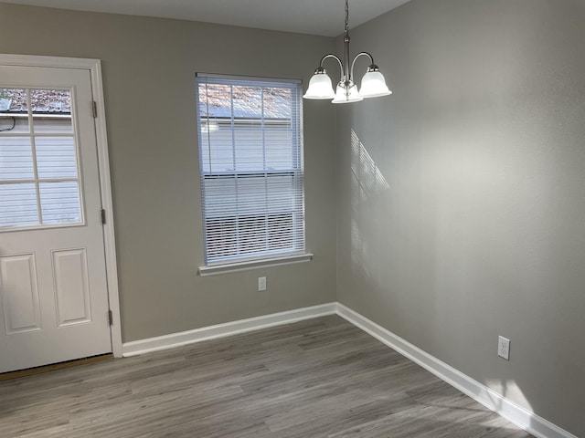 unfurnished dining area featuring wood-type flooring and an inviting chandelier