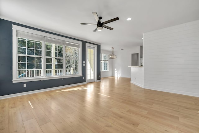 unfurnished living room featuring ceiling fan with notable chandelier and light hardwood / wood-style flooring