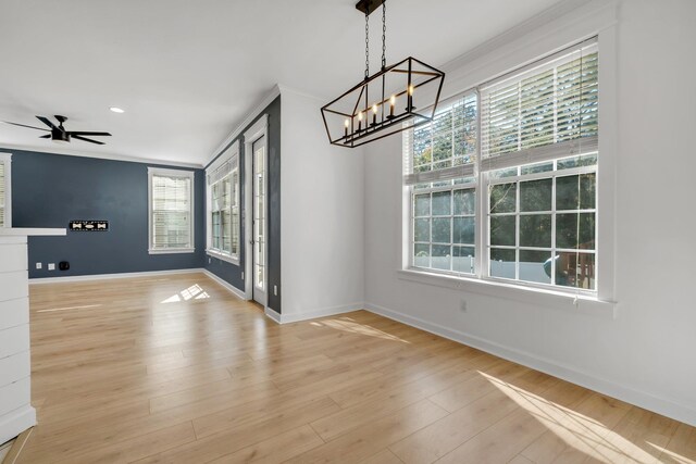 unfurnished dining area featuring ceiling fan with notable chandelier, light wood-type flooring, and crown molding