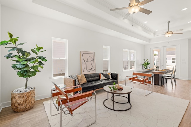 living room featuring ceiling fan, a raised ceiling, crown molding, light wood-type flooring, and french doors