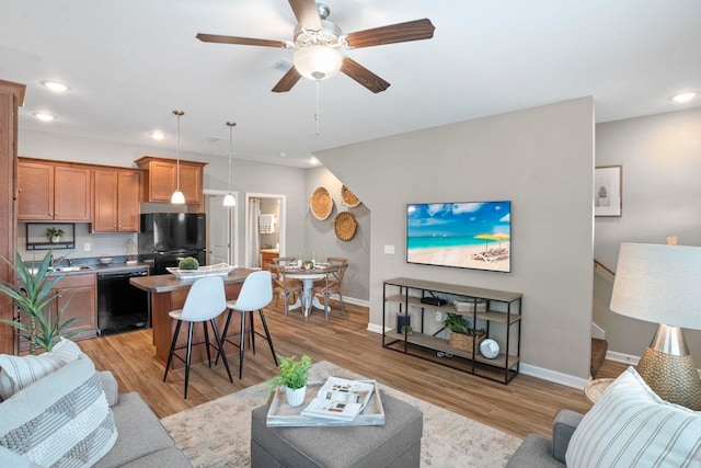 living room with ceiling fan, sink, and light wood-type flooring