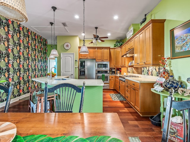 kitchen with appliances with stainless steel finishes, sink, hanging light fixtures, dark wood-type flooring, and a center island with sink