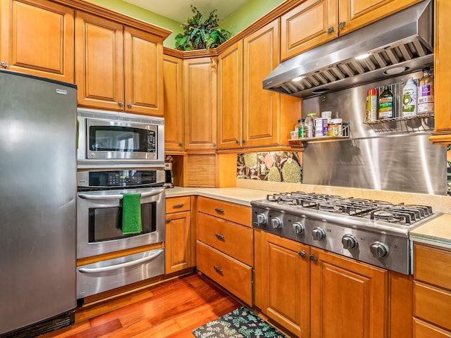 kitchen featuring stainless steel appliances, range hood, and wood-type flooring