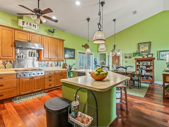 kitchen with pendant lighting, lofted ceiling, a breakfast bar, stainless steel gas cooktop, and an island with sink