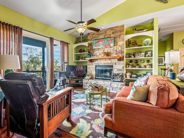 living room with built in shelves, ceiling fan, wood-type flooring, and a stone fireplace