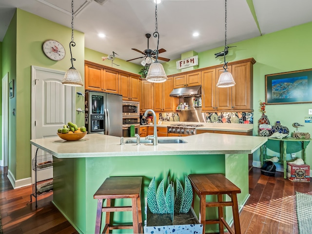 kitchen with a large island with sink, appliances with stainless steel finishes, sink, and decorative light fixtures