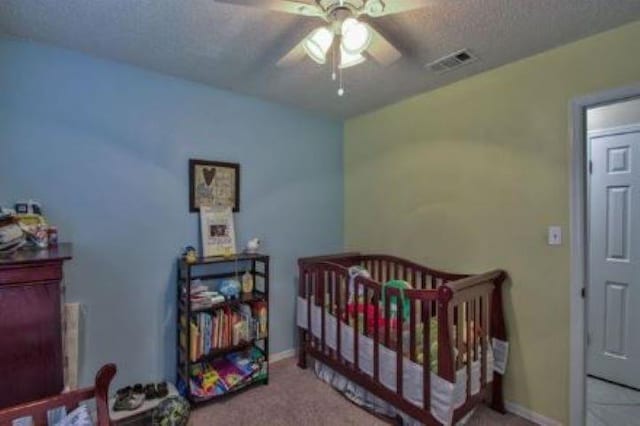 bedroom with ceiling fan, a textured ceiling, carpet, and a crib