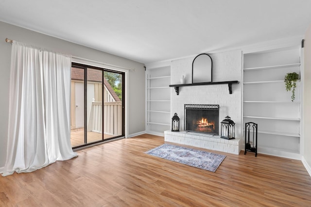 living room featuring built in shelves, hardwood / wood-style floors, and a brick fireplace