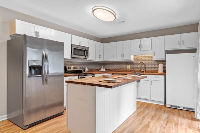 kitchen with wooden counters, white cabinets, light hardwood / wood-style flooring, a kitchen island, and stainless steel appliances