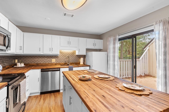 kitchen with light hardwood / wood-style floors, stainless steel appliances, sink, white cabinets, and butcher block countertops