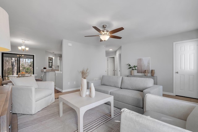 living area with light wood-type flooring, baseboards, and ceiling fan with notable chandelier