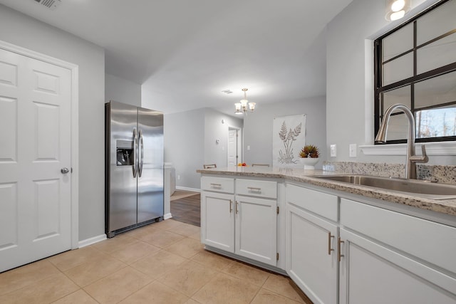 kitchen with stainless steel fridge, white cabinets, a chandelier, a sink, and light tile patterned flooring