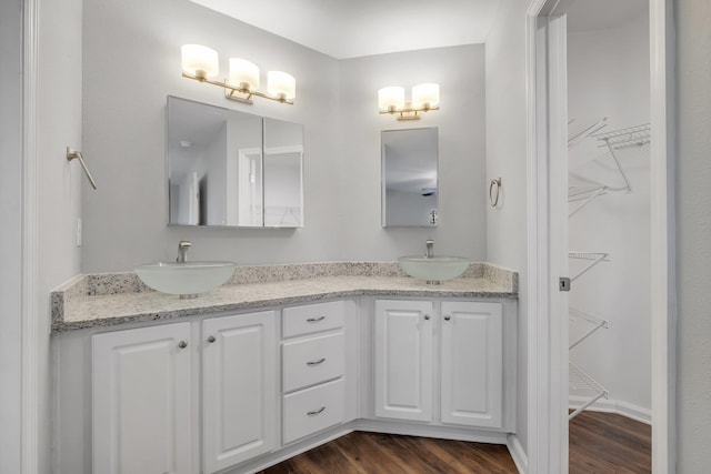 full bath with a walk in closet, a sink, and wood finished floors