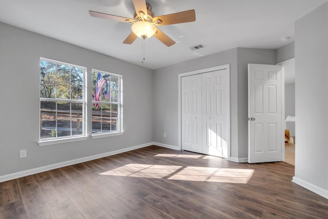 unfurnished bedroom featuring baseboards, visible vents, a ceiling fan, dark wood-type flooring, and a closet