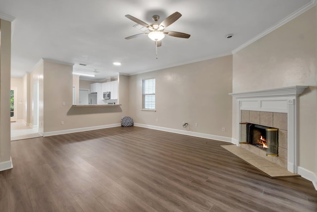 unfurnished living room with a ceiling fan, baseboards, a tiled fireplace, dark wood finished floors, and crown molding