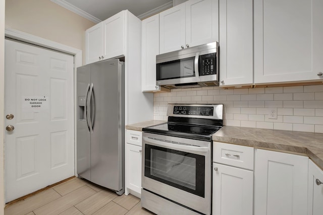 kitchen with tasteful backsplash, appliances with stainless steel finishes, white cabinets, and ornamental molding