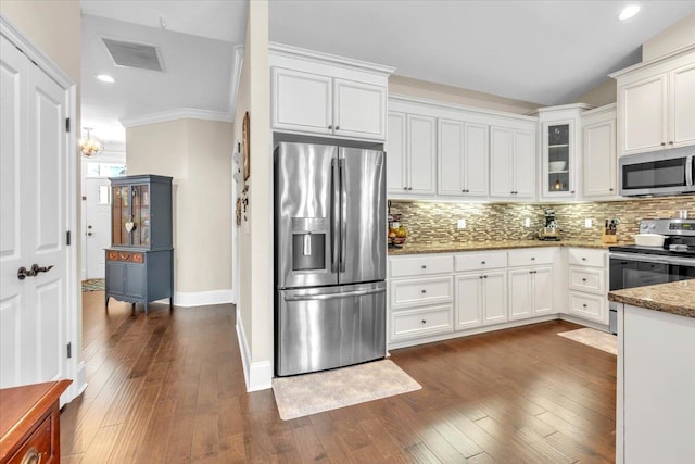 kitchen with dark wood-type flooring, dark stone counters, ornamental molding, appliances with stainless steel finishes, and white cabinetry