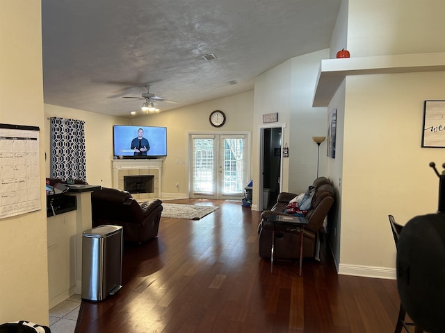 living room featuring lofted ceiling, a tile fireplace, ceiling fan, hardwood / wood-style floors, and french doors